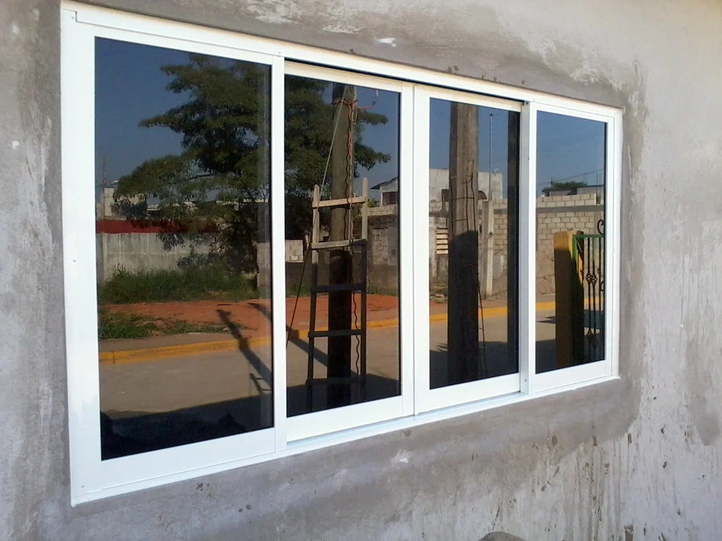 Técnico experto de RHS Window Repair ajustando un mecanismo de ventana moderna con vistas a un paisaje soleado en España.